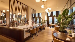 A modern hotel lobby with a bar area, seating arrangements, and large windows offering city views.