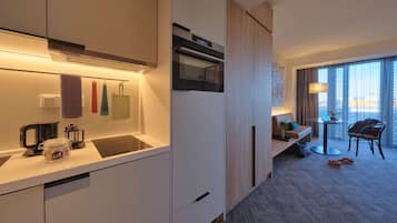 Une chambre d’hôtel moderne dotée d’une kitchenette, d’un coin salon avec une table et des chaises, et d’une grande fenêtre offrant une vue dégagée.