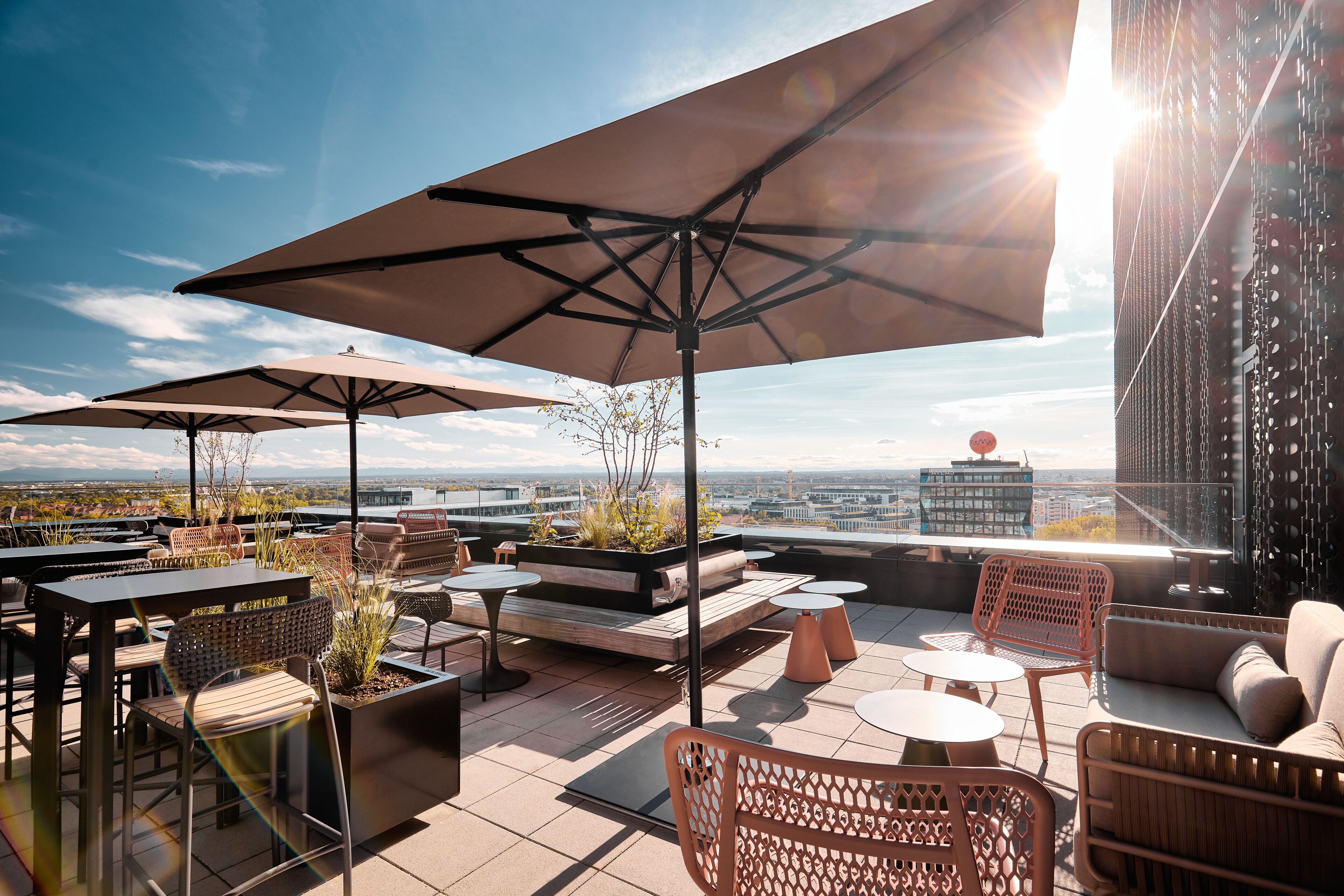 Terraço no telhado com área de estar ao ar livre, guarda-sóis e vista para a paisagem urbana.