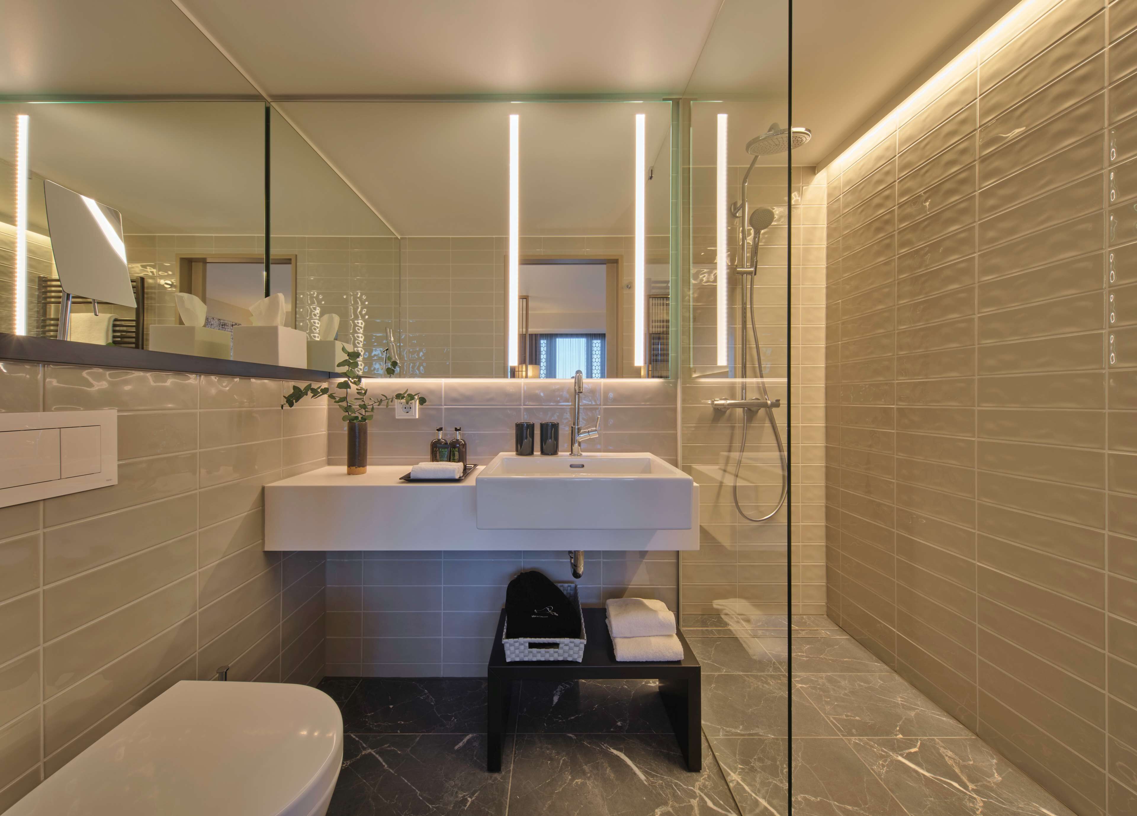 A modern bathroom with a glass shower enclosure, a white sink, and a black marble floor.