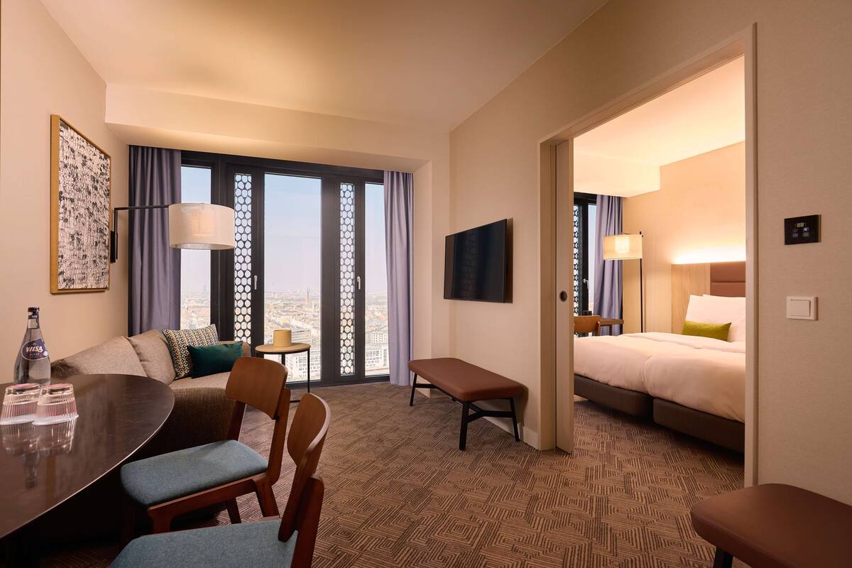 Ein Hotelzimmer mit Essbereich, einem Bett, einem Fernseher und Blick auf die Stadt.