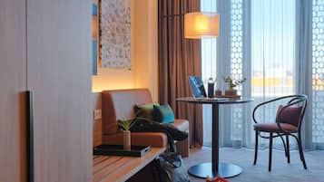 A hotel room with a sofa, a chair, a small table with a lamp, a laptop, and a plant.