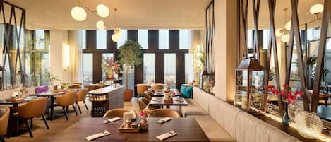 A modern restaurant with high ceilings, large windows, and a variety of seating options including tables and a long bench.