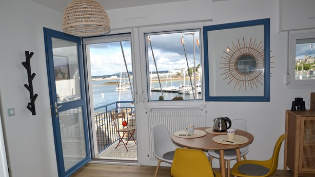 Spiseområde med udsigt over lystbådehavnen, et rundt bord med stole, en hængende lampe og et skab.