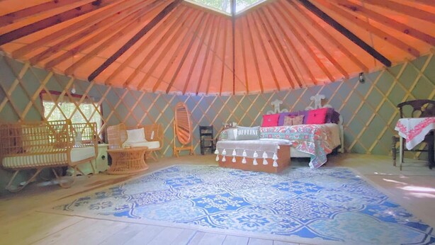 Una yurt con un lucernario centrale, un letto con una coperta colorata e un tappeto decorato.