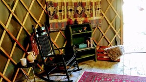 Un interno rustico con un pannello di legno a griglia, una poltrona a dondolo, un tavolino con una tazza e uno scaffale con oggetti decorativi.