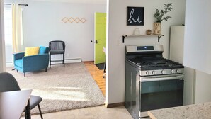 A modern kitchen with a stove, a dining area with a table and chairs, and a living area with a sofa and a chair.