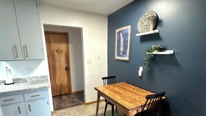 A dining area with a wooden table and chairs, a kitchen with light blue cabinets, and a dark blue accent wall with a feather artwork and a woven basket.