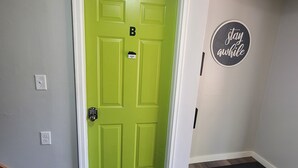 A green door with a keypad lock, a 'B' above it, and a 'stay safe' sign on the wall.