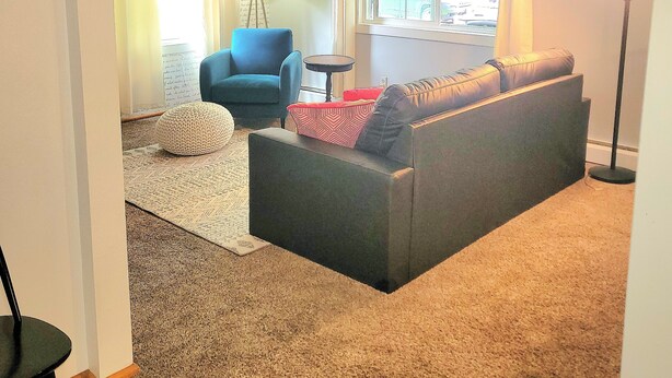 A living room with a grey sofa, a blue armchair, a floor lamp, and a patterned rug.