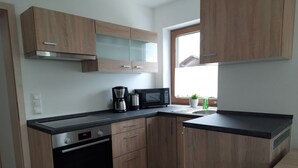 Una cucina compatta con mobili in legno, un forno Bosch, una macchina per il caffè e un forno a microonde.