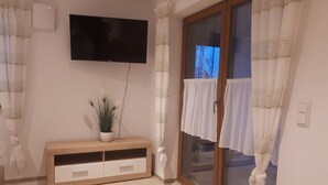 Un soggiorno con una TV a schermo piatto montata a parete, un tavolino consolle in legno con una pianta in vaso e una porta vetrata scorrevole con tende.