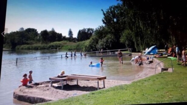 Un parco lungo il fiume con una panchina di legno, un tavolo da picnic e un'area giochi.