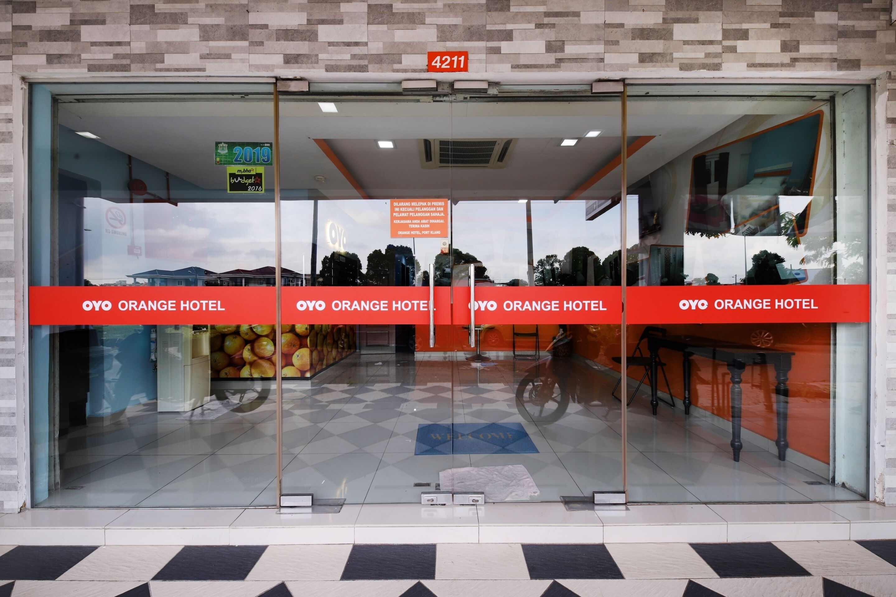 The entrance of OYO Orange Hotel with a checkered floor pattern and a welcome mat.