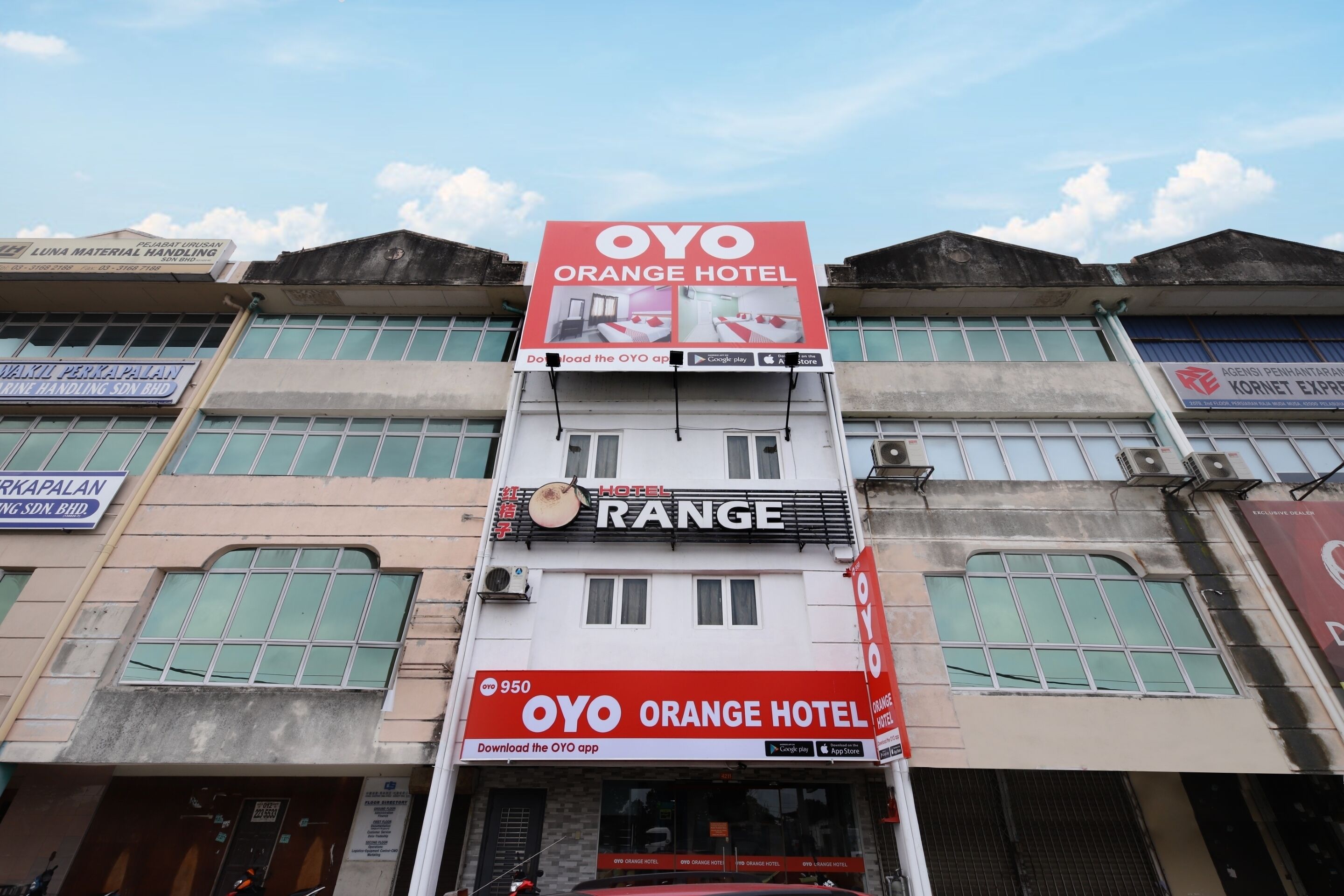 A hotel with a prominent OYO Orange Hotel sign, a Range hotel sign, and a Luna Material Handling sign.