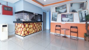 A hotel lobby with a reception desk, a wall with fruit images, and a seating area with two chairs and a small table. - OYO 90296 Red Orange Hotel Port Klang (Pelabuhan Klang)