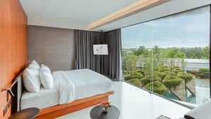 A modern bedroom with a large bed, a small table, and a view of a landscaped area through large windows. - Livist Resort Phetchabun (Phetchabun)
