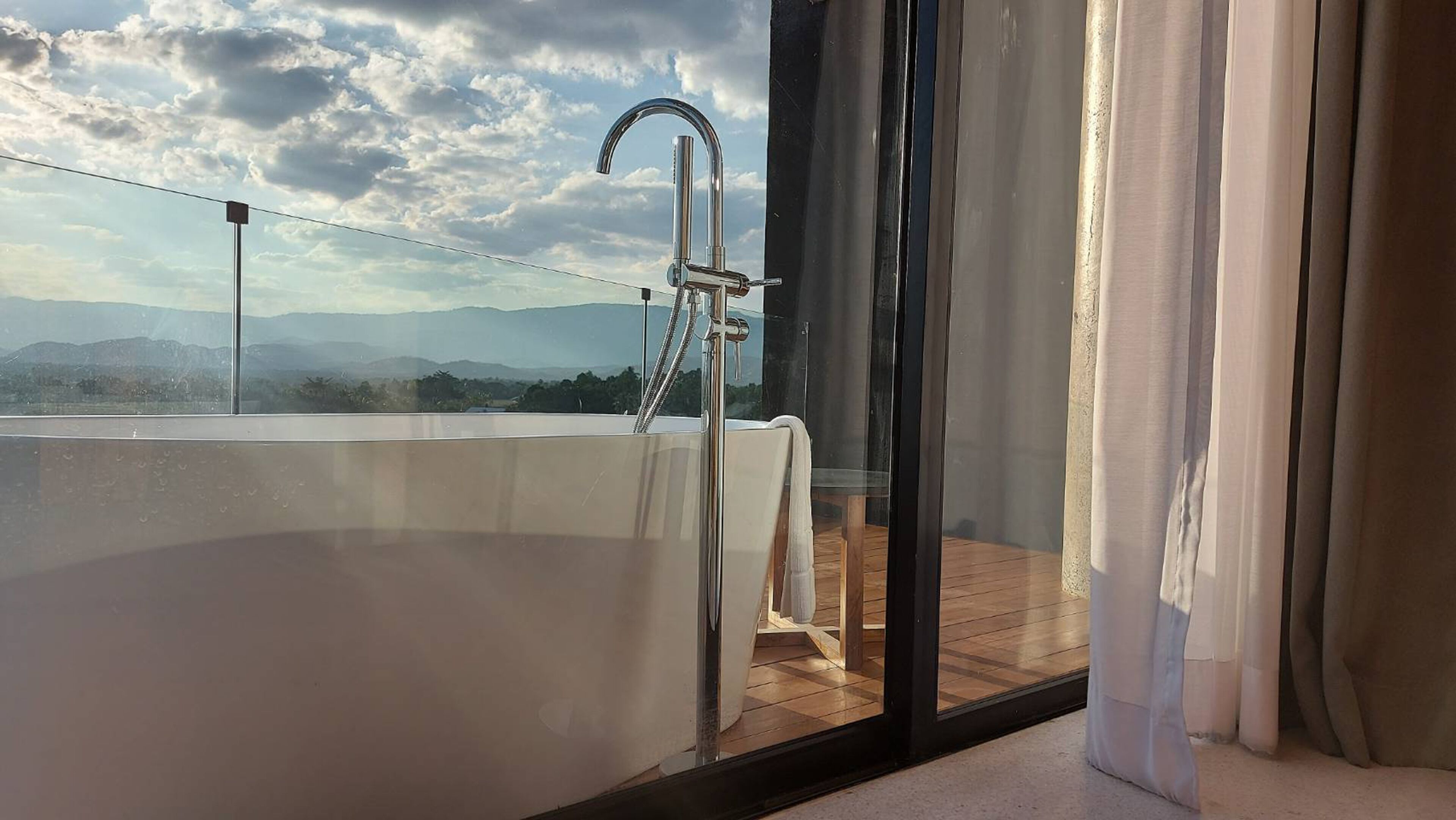 A balcony with a glass barrier, a metal faucet, and a view of distant mountains.