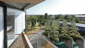 A modern balcony with a glass railing overlooking a landscaped garden and residential buildings.