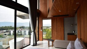 A modern hotel room with a large window, a bathtub, a sofa, and a small table. - Livist Resort Phetchabun (Phetchabun)