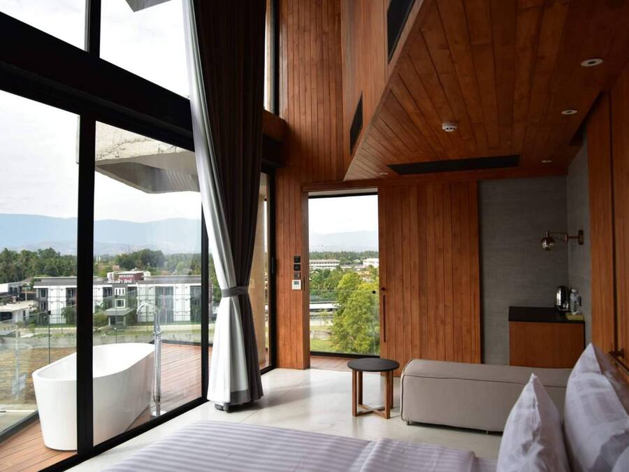 A modern hotel room with a large window, a bathtub, a sofa, and a small table.