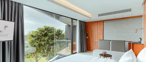 A modern hotel room with a large bed, a small table, a seating area, and a view of the outdoors.
