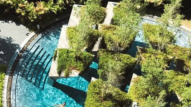A swimming pool with a person swimming, surrounded by greenery and modern architecture. - Livist Resort Phetchabun (Phetchabun)