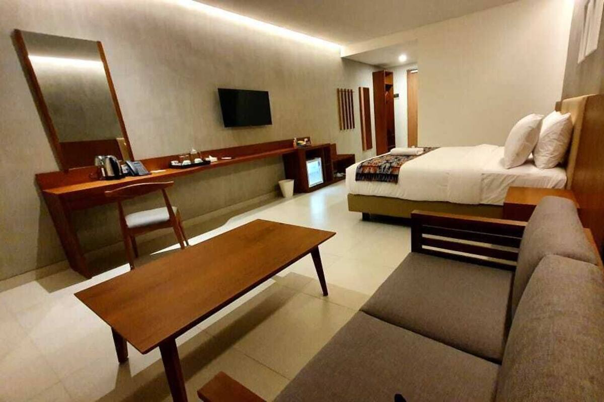 Ein Hotelzimmer mit Bett, Schreibtisch, Sessel, Sofa und Fernseher.