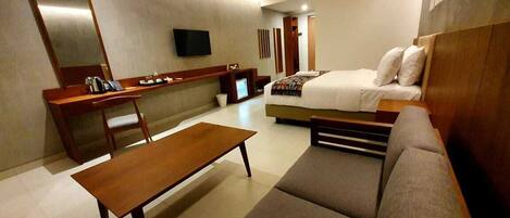 Una habitación de hotel con cama, escritorio, silla, sofá y televisor.