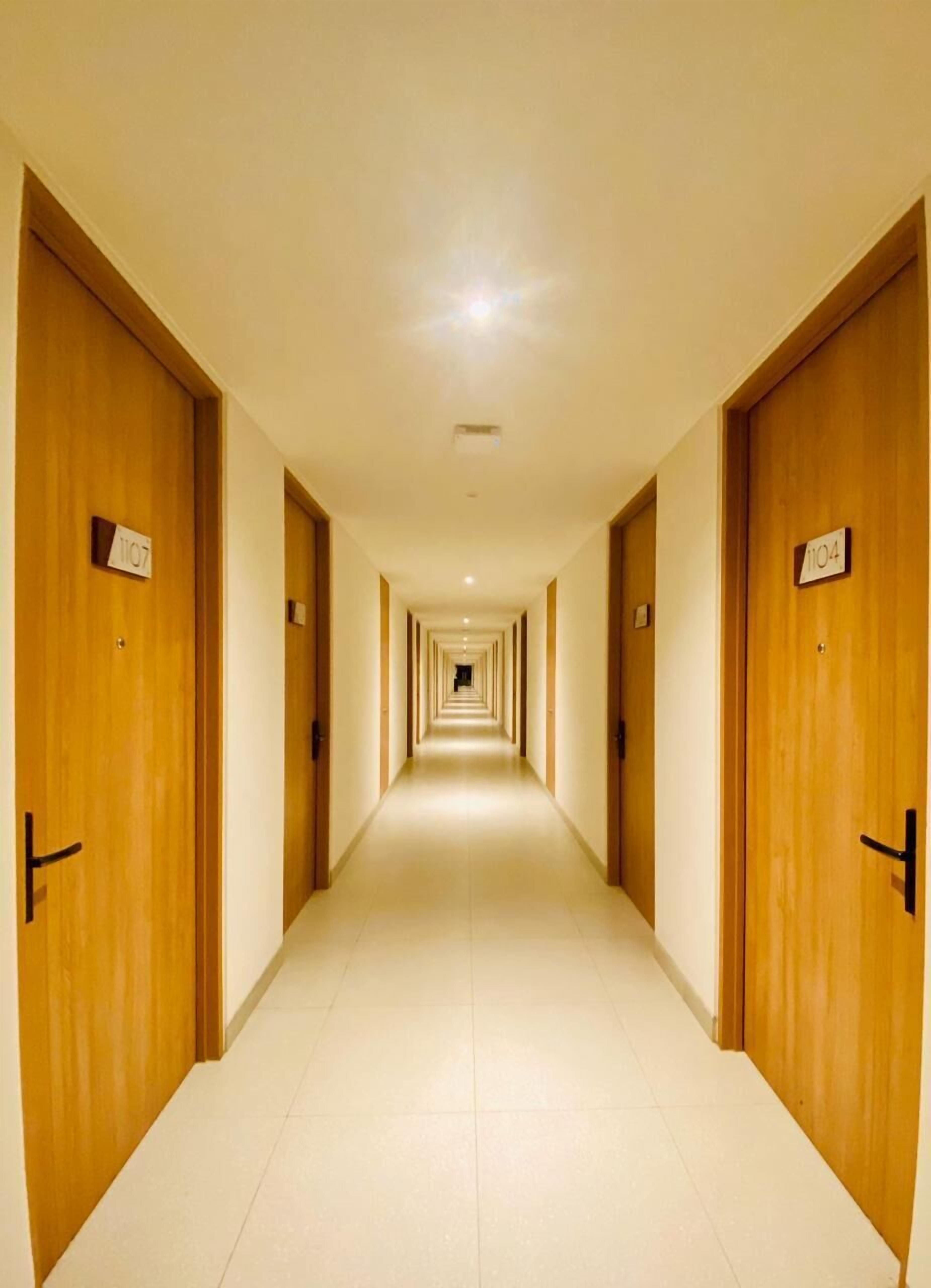 A long, narrow hotel corridor with wooden doors on both sides, each marked with a room number.