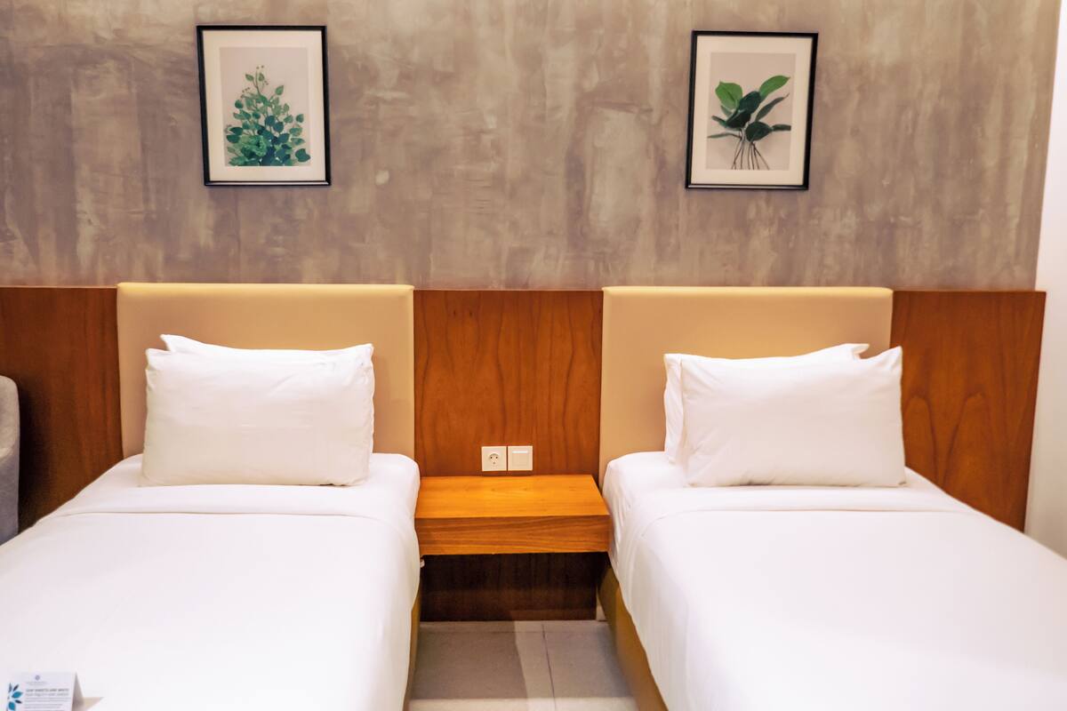 Ein Hotelzimmer mit zwei Betten, Holzkopfteilen und zwei gerahmten Pflanzenbildern an der Wand.