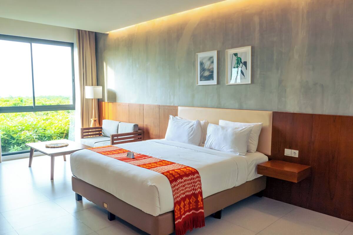Ein Hotelzimmer mit einem großen Bett, einem kleinen Schreibtisch und Blick auf Grünfläche.