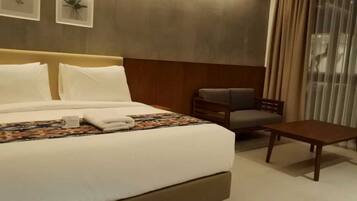 A hotel room with a large bed, a chair, a small table, and a window with curtains.