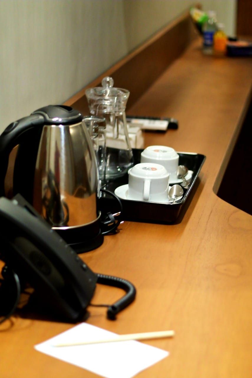 Una reception d'albergo con un telefono, una macchina del caffè e un vassoio con tazze e un bicchiere.