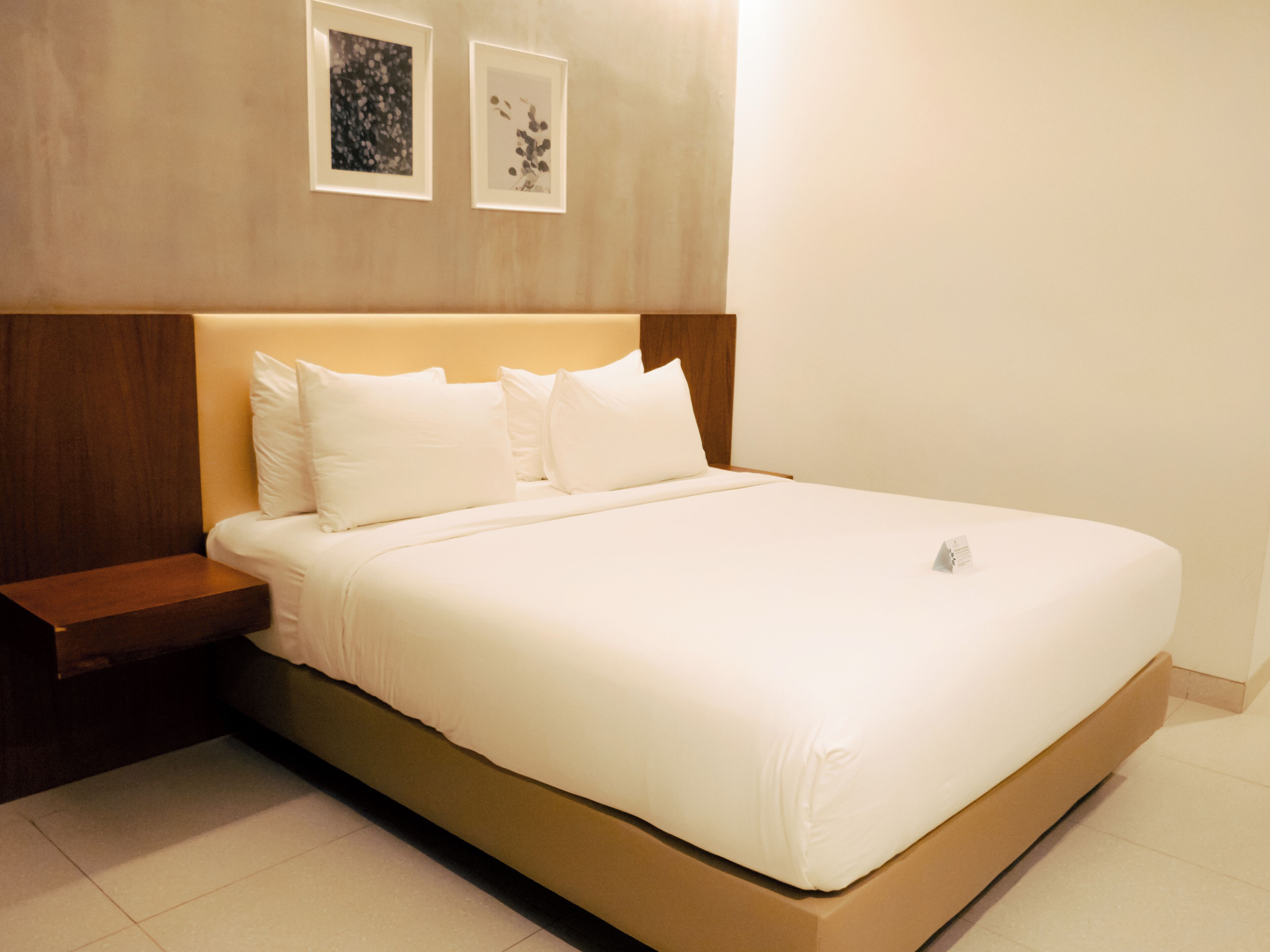 A modern bedroom with a large bed, wooden headboard, and two framed pictures on the wall.