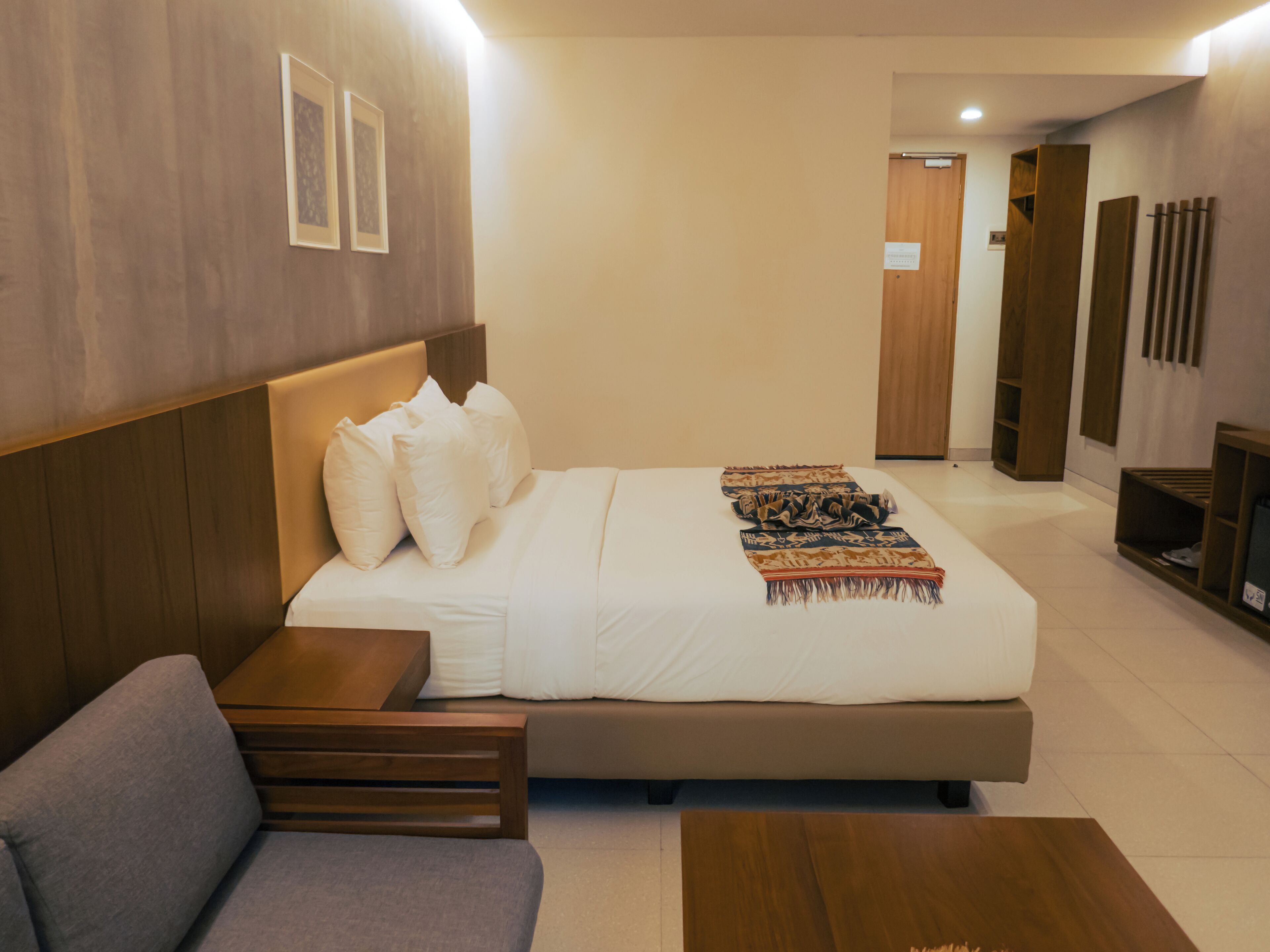 A modern hotel room with a large bed, a sofa, a wooden headboard, and a small table.