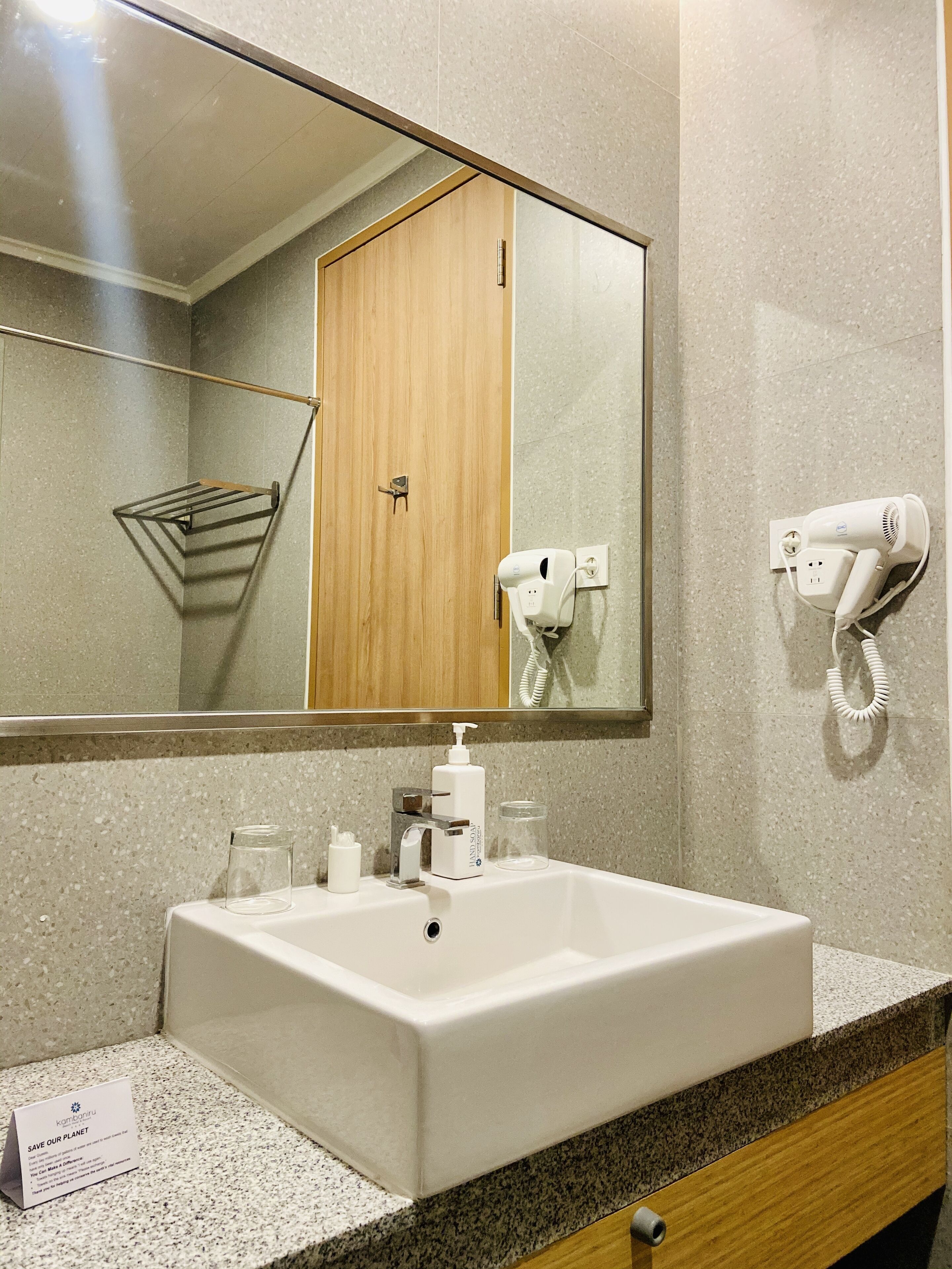 A bathroom with a large mirror, a sink, a towel rack, a hairdryer, and a soap dispenser.