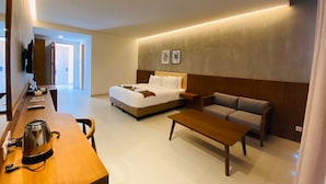 Een moderne hotelkamer met een bed, een bank, een salontafel en een bureau met een waterkoker.
