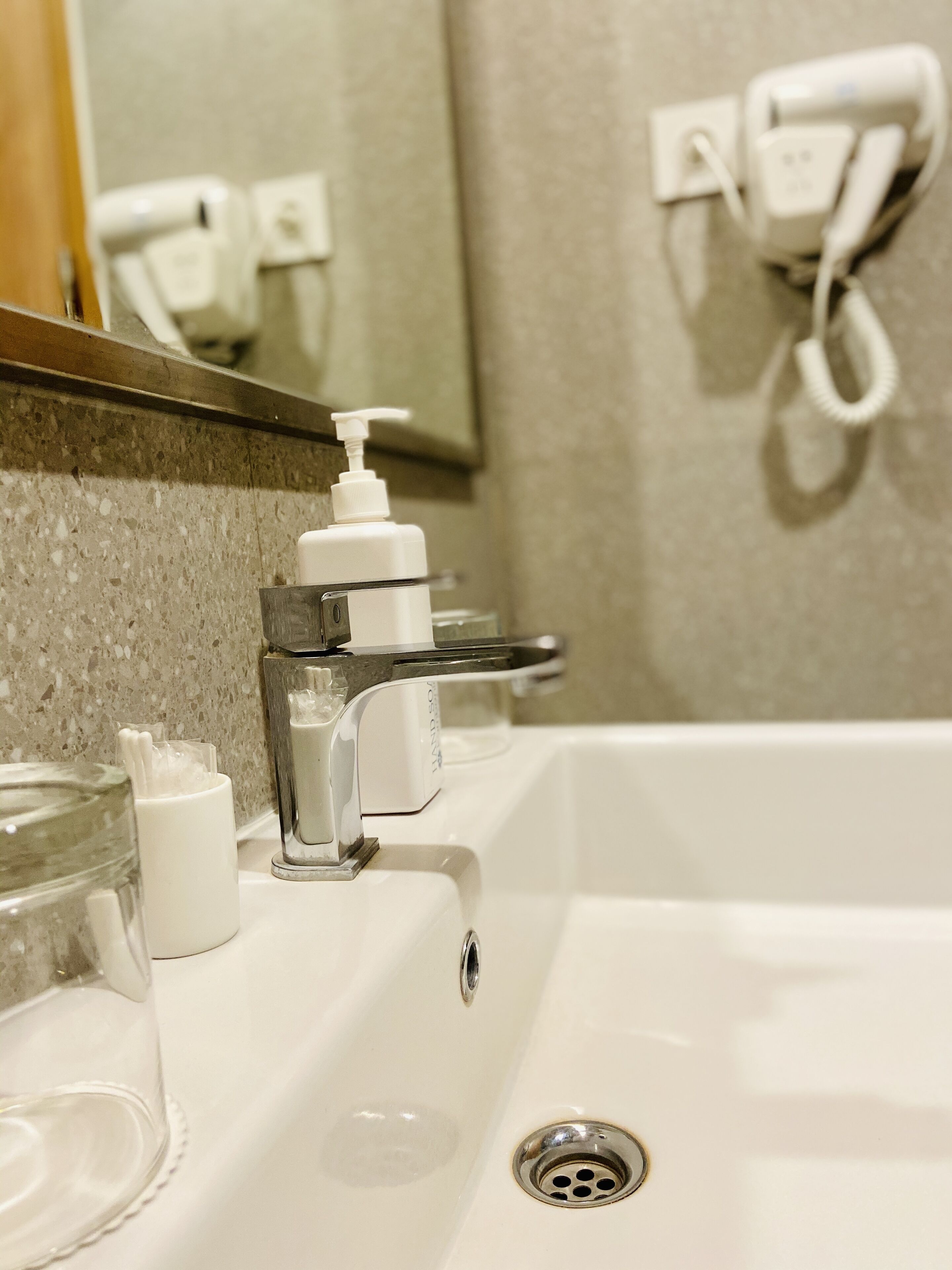 Un lavabo de salle de bain avec un distributeur de savon transparent en verre, un miroir au-dessus et un téléphone blanc fixé au mur.