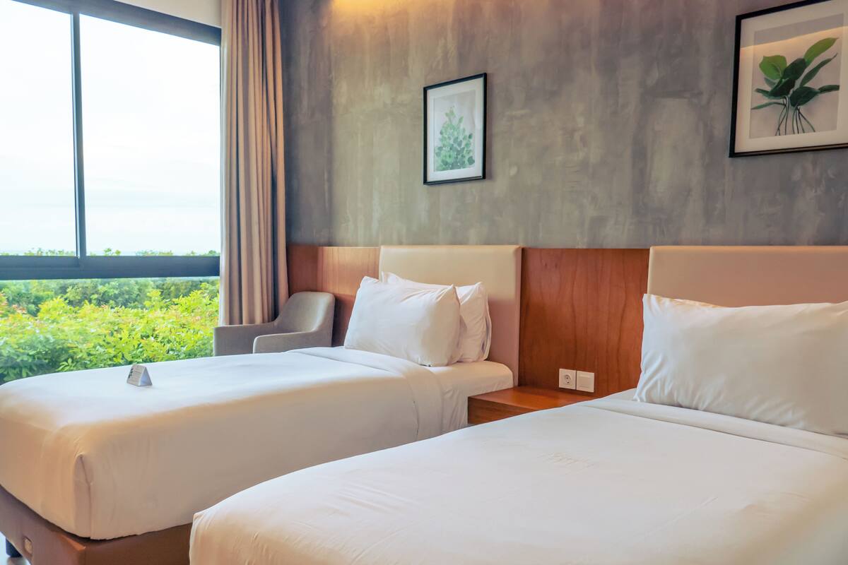 Ein Hotelzimmer mit zwei Betten, einem Sessel und Blick auf Grün.