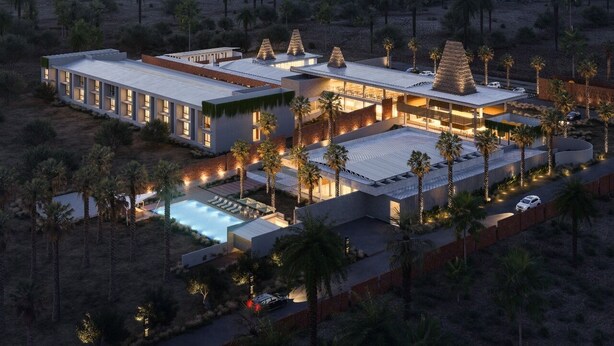 Een modern resort met meerdere gebouwen, een zwembad en palmbomen.