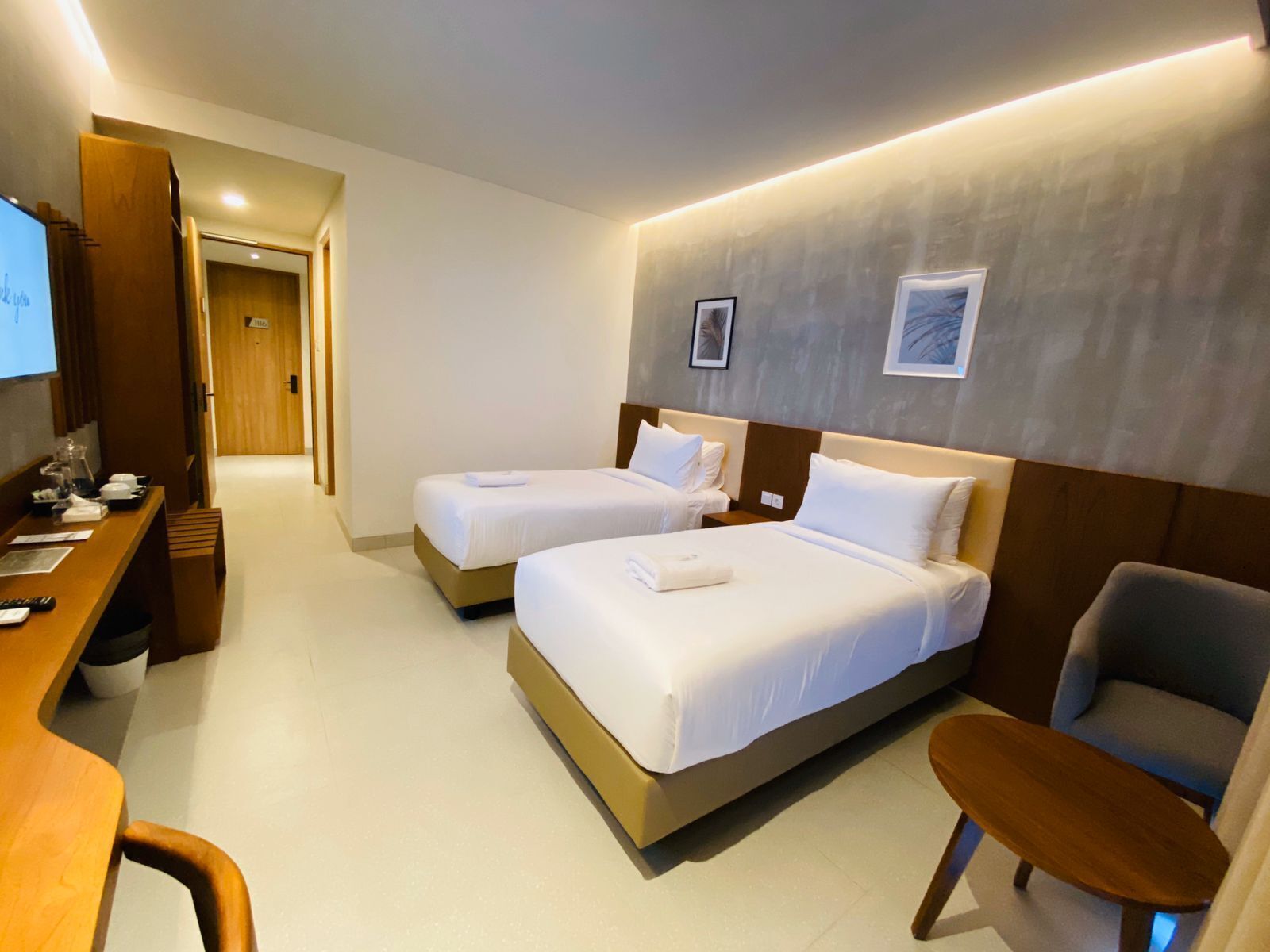 Quarto de hotel com duas camas, uma escrivaninha com computador, uma cadeira e uma televisão.