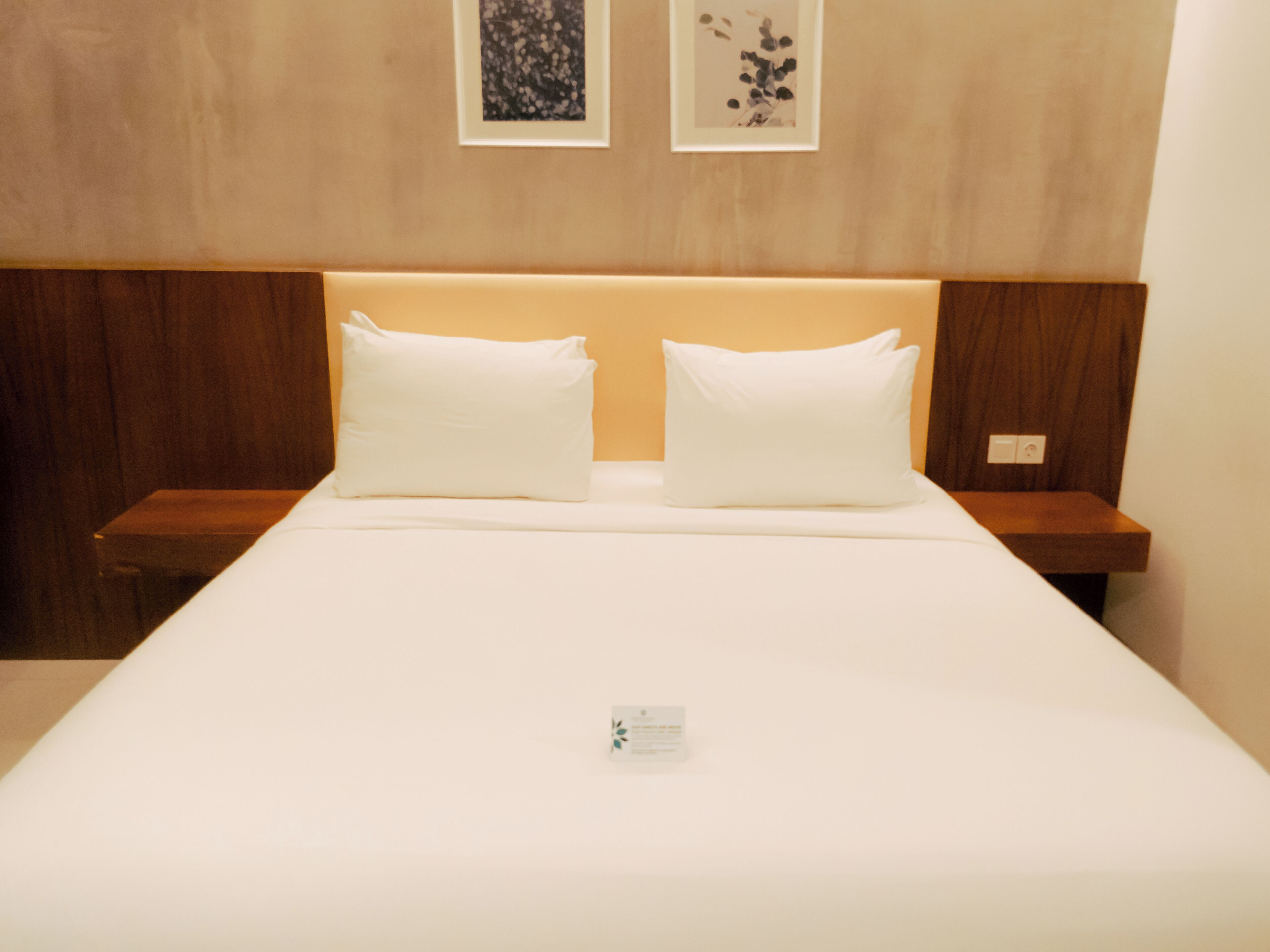 Une chambre d’hôtel avec un grand lit, deux oreillers blancs, une tête de lit en bois et deux tables de chevet.