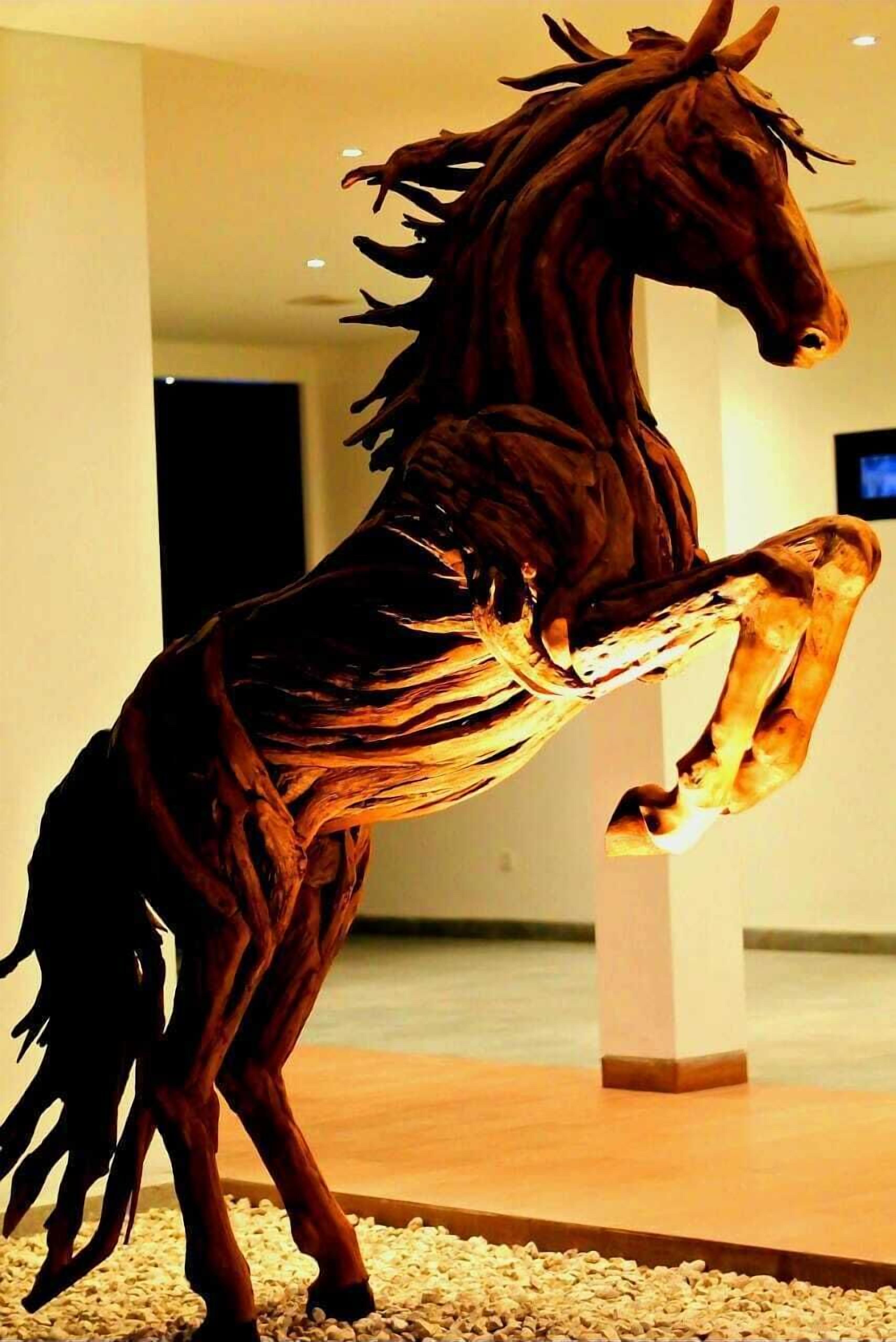 A sculpture of a horse in a room with a wooden floor and a white pillar.