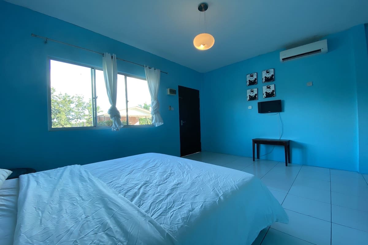 A bedroom with a bed, a window with curtains, an air conditioning unit, a wall-mounted TV, and a small table.