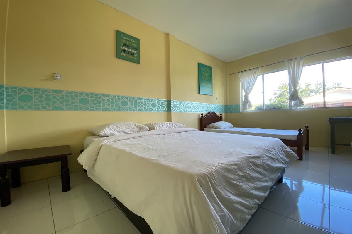 A hotel room with two beds, a bench, and a window with curtains.