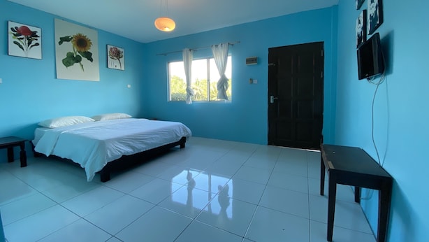 A bedroom with a bed, a window with curtains, a door, and a wall-mounted TV. - Hotel O Rb Homestay & Farms (Kuching)