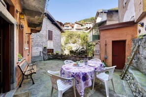 A courtyard with stone walls, a table with a purple tablecloth, and white chairs.