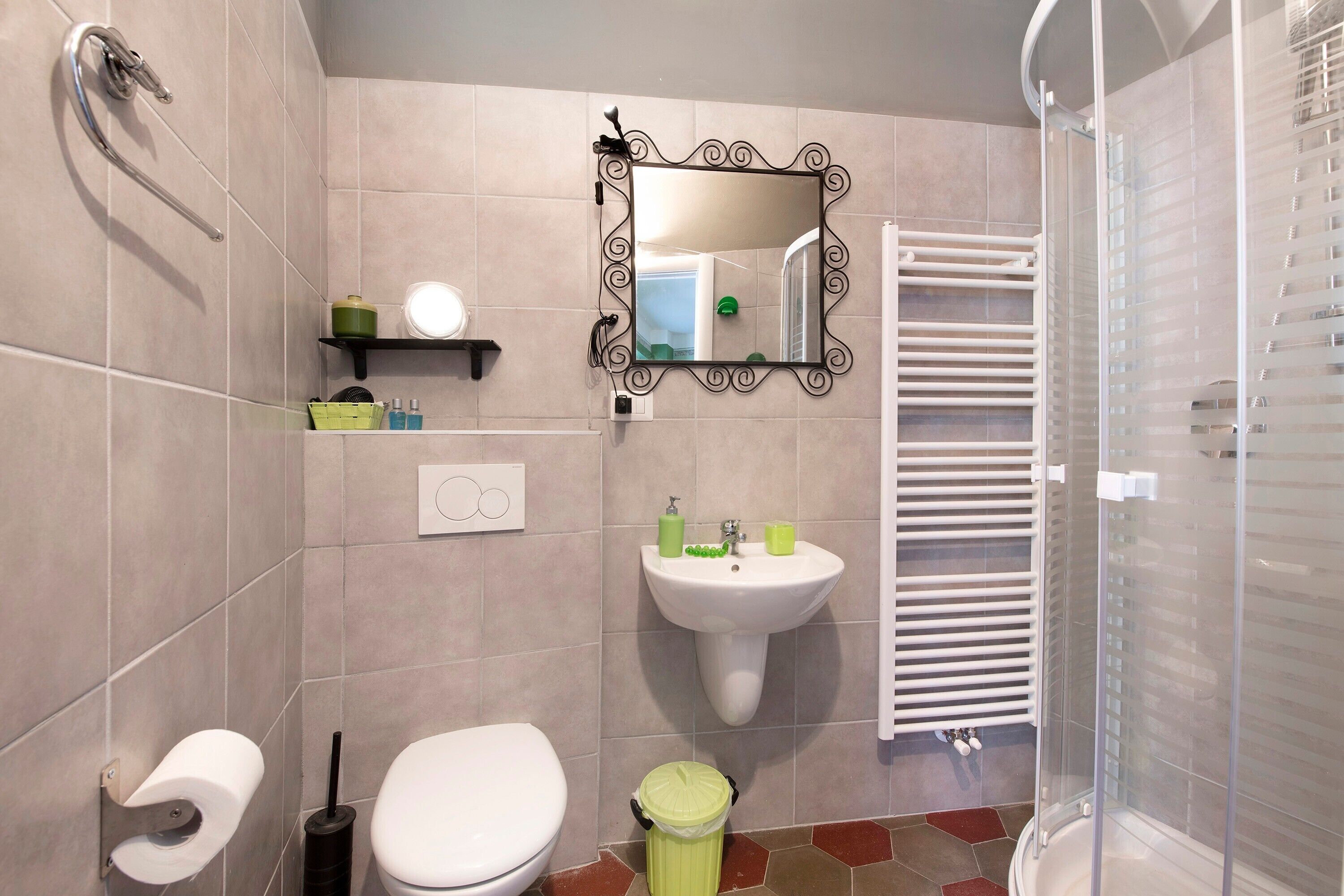 A bathroom with a toilet, sink, shower, and a mirror with a decorative frame.