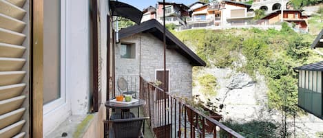A balcony with a table and chairs, overlooking a hillside with buildings.